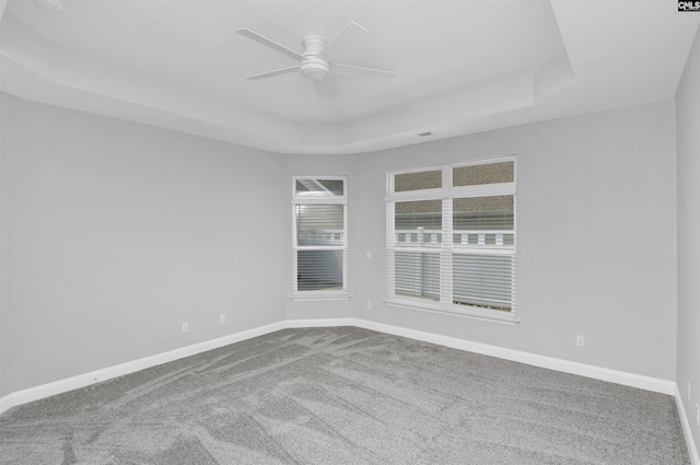 unfurnished room with a ceiling fan, carpet flooring, a tray ceiling, and baseboards