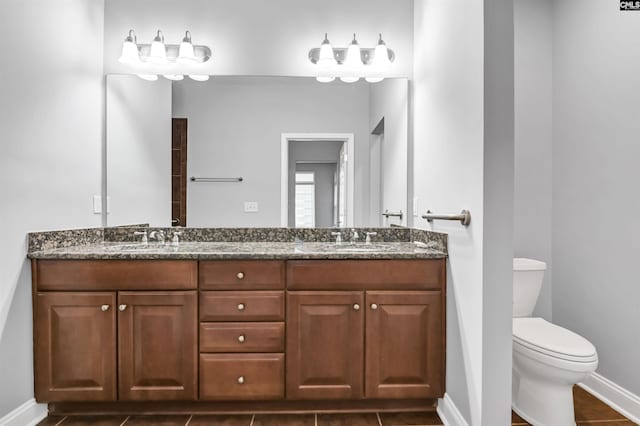 bathroom featuring a sink, double vanity, toilet, and baseboards