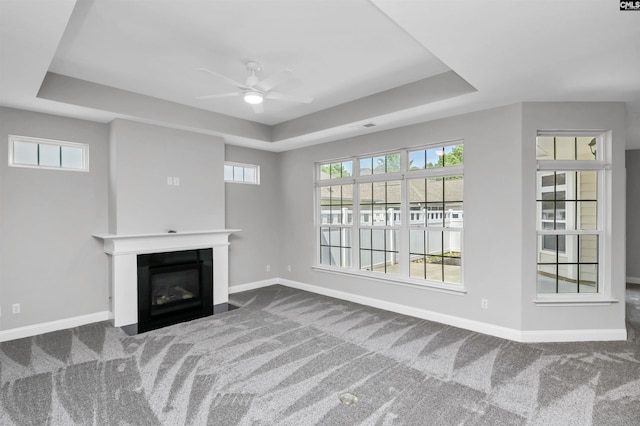 unfurnished living room featuring ceiling fan, a raised ceiling, and carpet