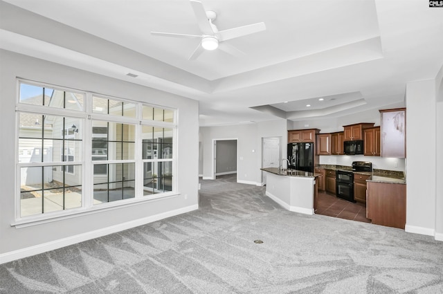 unfurnished living room featuring baseboards, a raised ceiling, dark carpet, and a sink