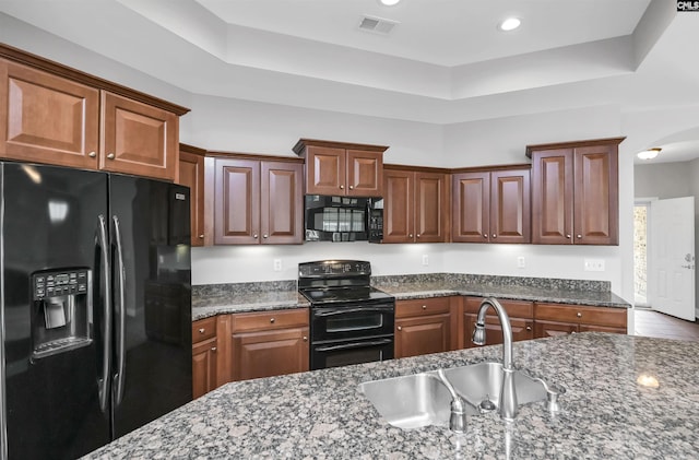 kitchen featuring visible vents, a sink, dark stone countertops, arched walkways, and black appliances