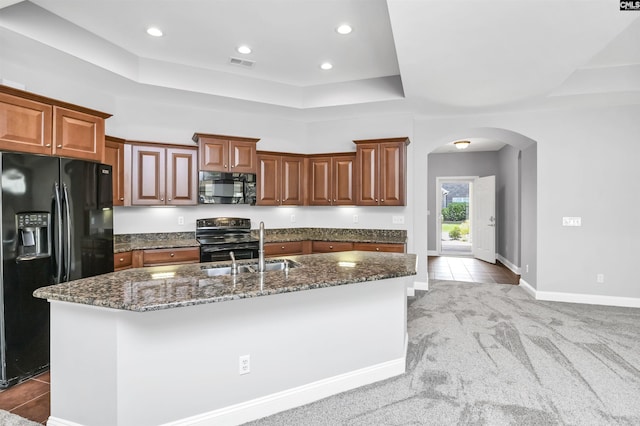 kitchen featuring a tray ceiling, visible vents, dark stone countertops, arched walkways, and black appliances