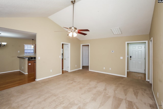 unfurnished living room with baseboards, visible vents, ceiling fan, vaulted ceiling, and light colored carpet