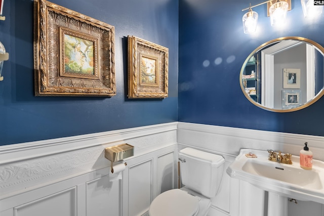 half bath featuring a sink, toilet, a decorative wall, and a wainscoted wall