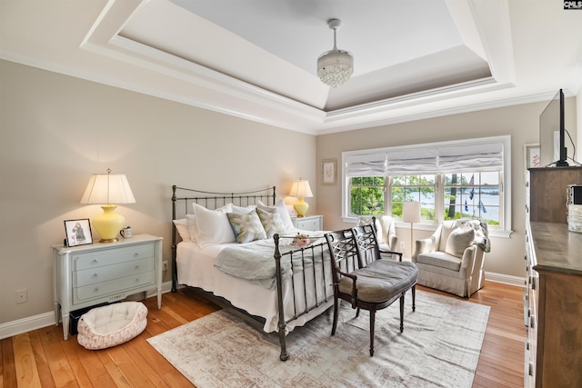 bedroom featuring ornamental molding, a raised ceiling, light wood-style floors, and baseboards