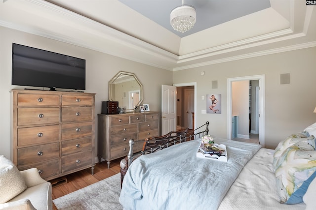 bedroom featuring an inviting chandelier, wood finished floors, a raised ceiling, and ornamental molding
