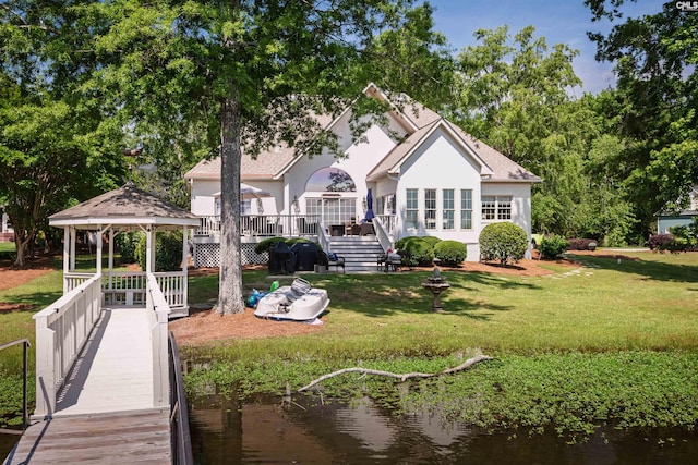 back of property featuring a yard, a deck with water view, stucco siding, a shingled roof, and a gazebo