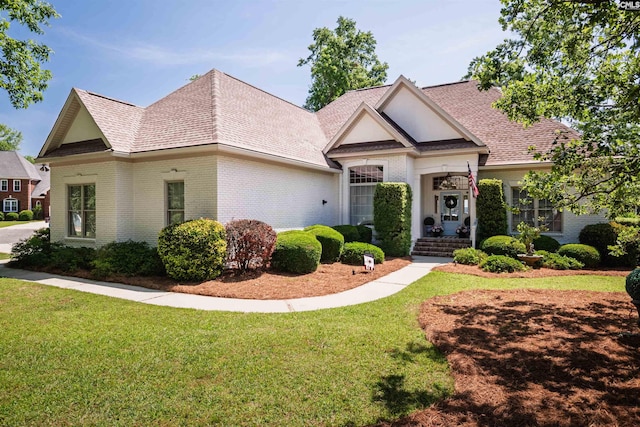 view of front of property with roof with shingles, brick siding, and a front yard