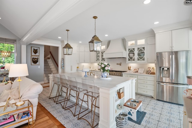 kitchen featuring a breakfast bar area, range, custom range hood, stainless steel fridge with ice dispenser, and white cabinets