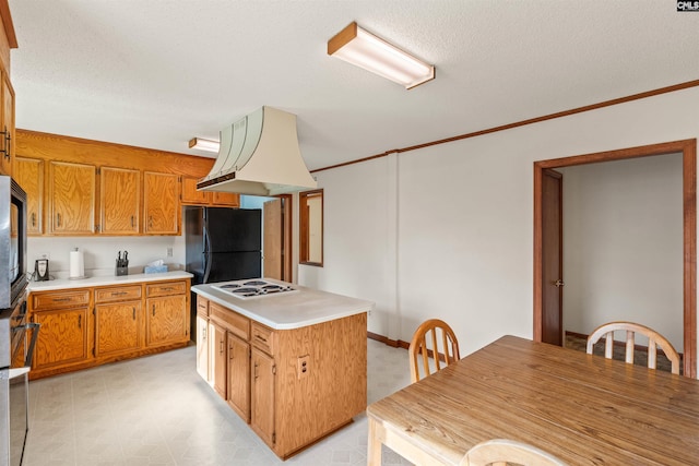 kitchen featuring brown cabinets, freestanding refrigerator, crown molding, light countertops, and white electric cooktop