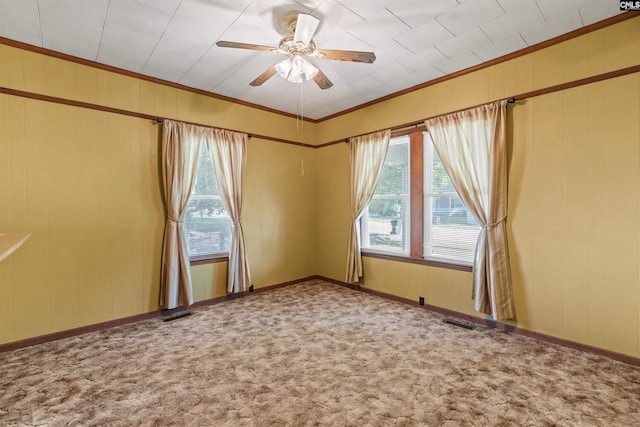carpeted spare room with ornamental molding, visible vents, wooden walls, a ceiling fan, and baseboards