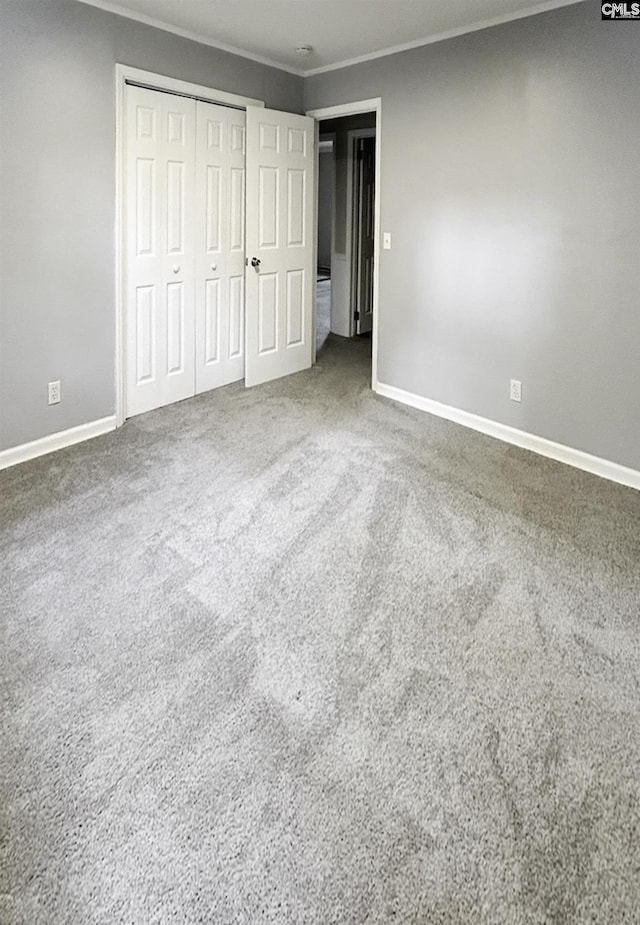 unfurnished bedroom with carpet floors, ornamental molding, baseboards, and a closet