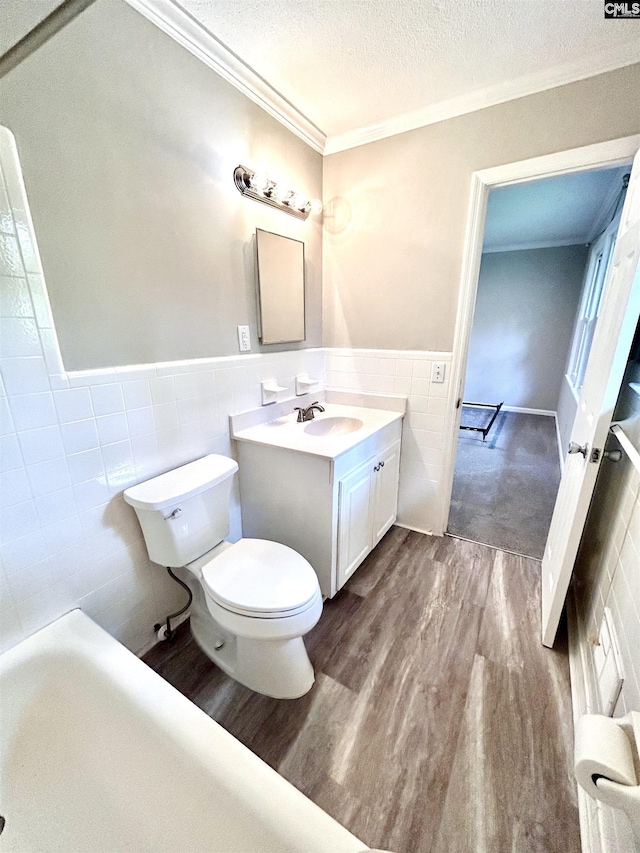 bathroom featuring toilet, wood finished floors, tile walls, a textured ceiling, and ornamental molding