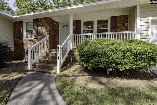 doorway to property featuring a porch and brick siding