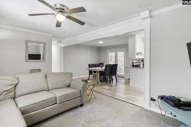 living room featuring light colored carpet, crown molding, ceiling fan, baseboards, and light wood-style floors