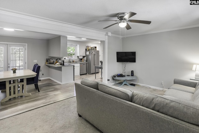 living room with crown molding, baseboards, ceiling fan, and light wood-style floors