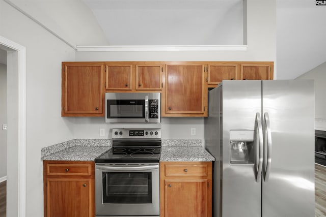 kitchen with appliances with stainless steel finishes, brown cabinetry, and light stone countertops