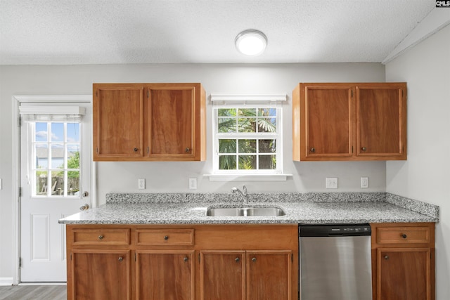 kitchen with wood finished floors, stainless steel dishwasher, brown cabinetry, and a sink