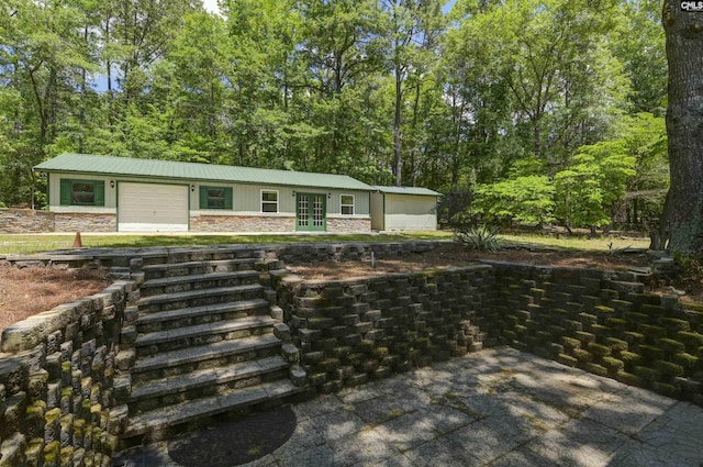view of front of property featuring stone siding, metal roof, french doors, and a garage