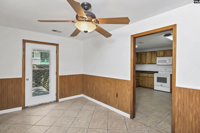 empty room featuring a ceiling fan, wainscoting, visible vents, light tile patterned flooring, and wooden walls