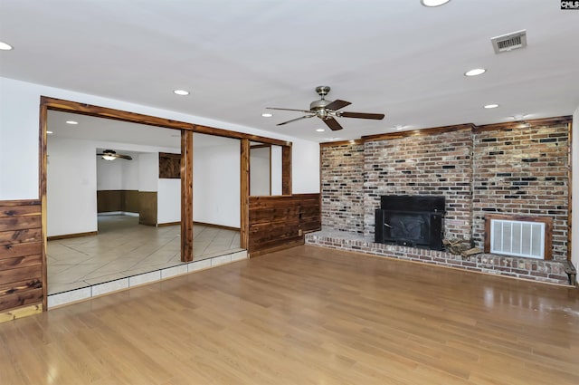 unfurnished living room with a fireplace, a ceiling fan, visible vents, and wood finished floors