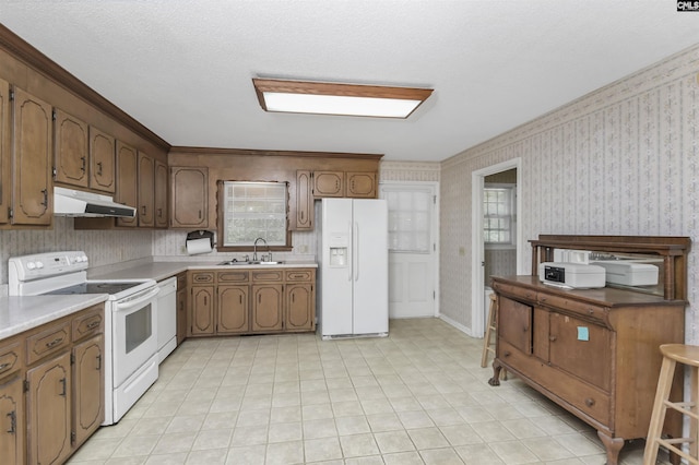 kitchen featuring white appliances, a sink, wallpapered walls, and under cabinet range hood