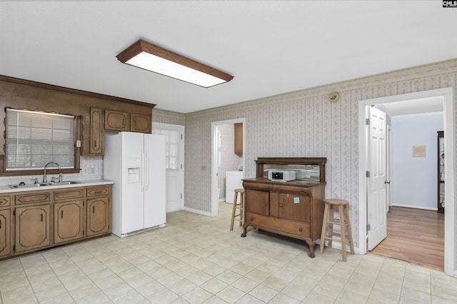 kitchen featuring a sink, wallpapered walls, white refrigerator with ice dispenser, washer / dryer, and light countertops