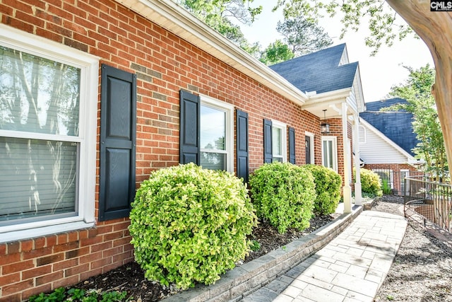 view of side of home featuring brick siding, roof with shingles, and fence