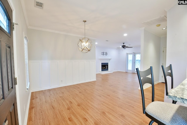 dining area with ceiling fan with notable chandelier, visible vents, a fireplace with raised hearth, crown molding, and light wood-style floors