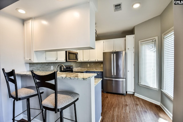 kitchen with dark wood-style flooring, visible vents, white cabinetry, a peninsula, and stainless steel appliances