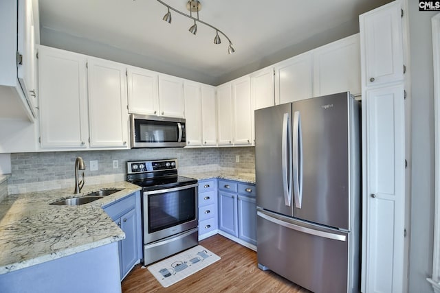kitchen with light stone countertops, a sink, backsplash, white cabinets, and appliances with stainless steel finishes