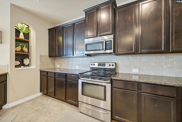 kitchen featuring tasteful backsplash, dark brown cabinets, baseboards, stainless steel appliances, and dark stone counters