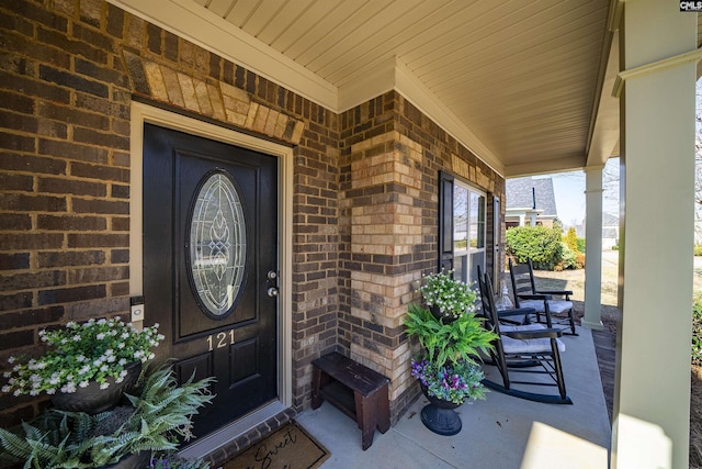 doorway to property featuring a porch and brick siding