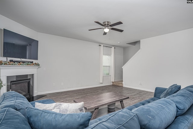 living room featuring a ceiling fan, a fireplace with flush hearth, wood finished floors, and baseboards
