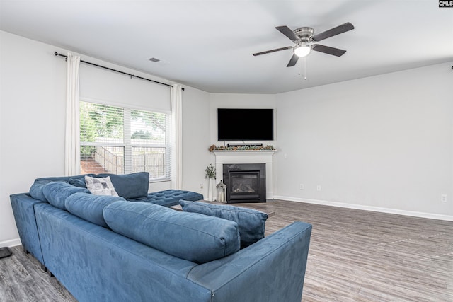 living room with wood finished floors, baseboards, a glass covered fireplace, and a ceiling fan