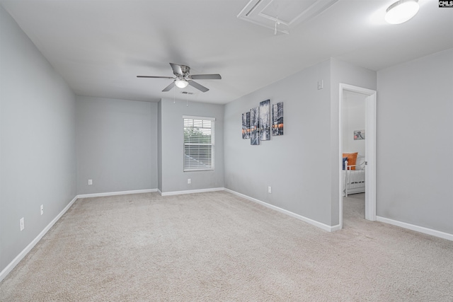 spare room with attic access, light colored carpet, a ceiling fan, and baseboards