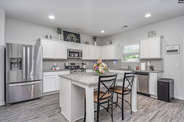 kitchen with stainless steel appliances, white cabinetry, wood finished floors, tasteful backsplash, and recessed lighting