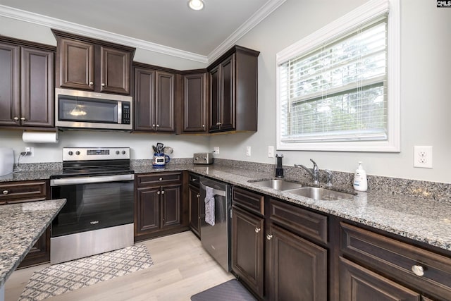 kitchen with appliances with stainless steel finishes, a sink, light wood-style flooring, dark brown cabinets, and dark stone counters