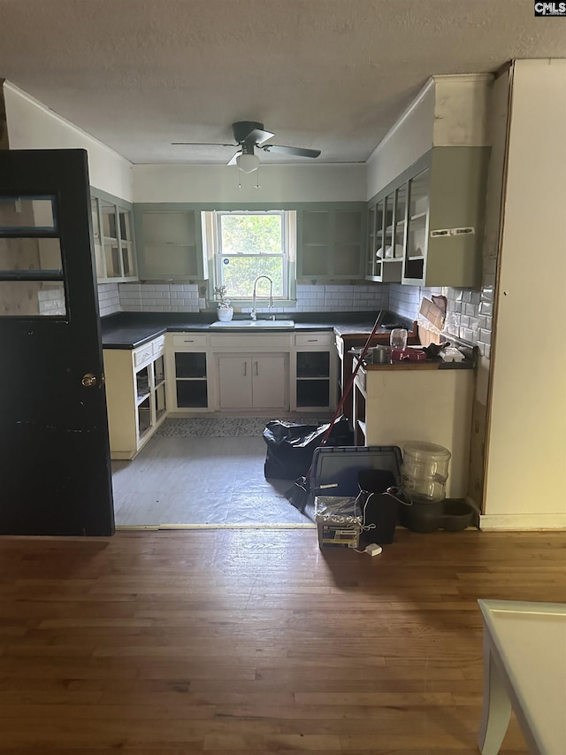 kitchen featuring open shelves, a sink, light wood-style floors, decorative backsplash, and a textured ceiling