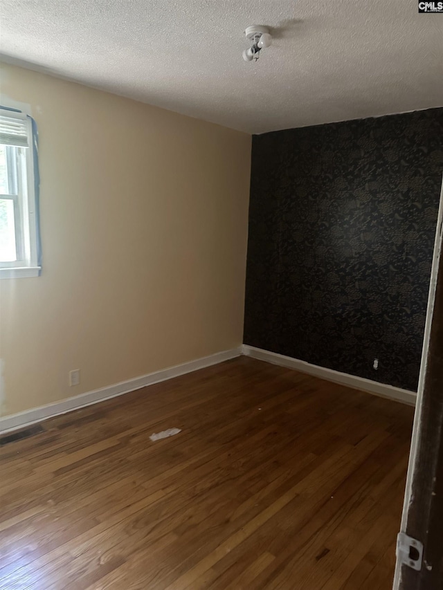 spare room with wood finished floors, a textured ceiling, and baseboards
