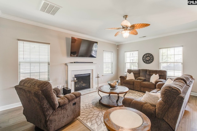 living area featuring a ceiling fan, ornamental molding, light wood-style floors, a fireplace, and baseboards