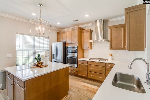kitchen with wall chimney range hood, a sink, appliances with stainless steel finishes, crown molding, and light wood-style floors