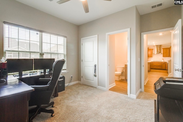 office space with light colored carpet, a ceiling fan, and baseboards
