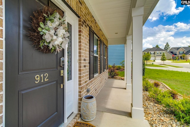 view of exterior entry with a porch, brick siding, and a residential view