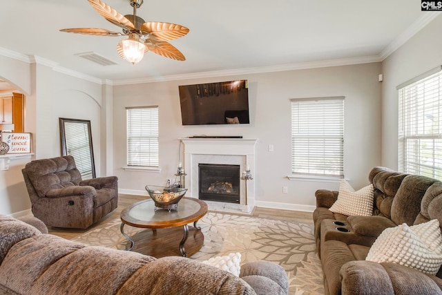 living area featuring ornamental molding, light wood-style flooring, a ceiling fan, baseboards, and a fireplace