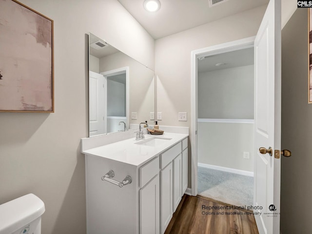 half bathroom featuring wood finished floors, vanity, and toilet