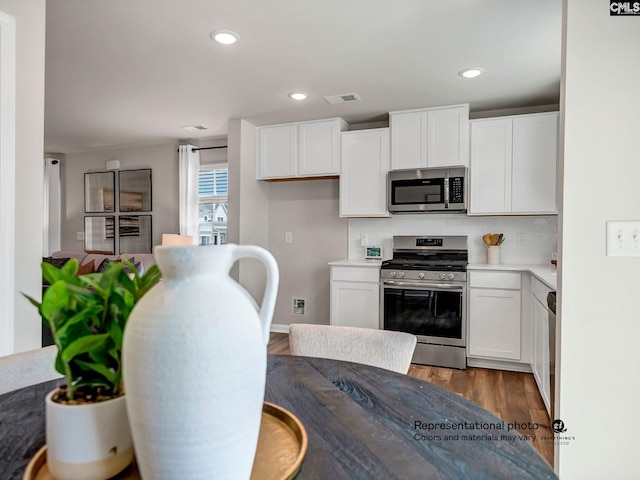 kitchen with stainless steel appliances, wood finished floors, white cabinets, backsplash, and recessed lighting