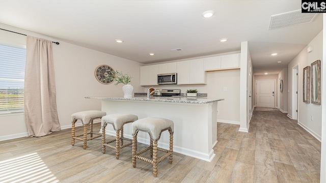 119 Shumard Ct, Columbia, SC 29203 - kitchen featuring stainless steel appliances, light wood finished floors, white cabinetry, light stone counters, and a breakfast bar