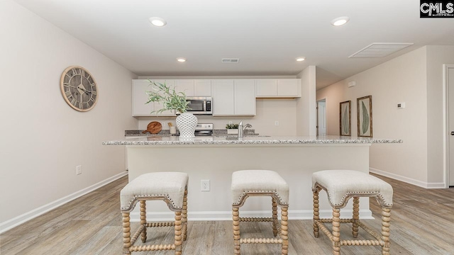 119 Shumard Ct, Columbia, SC 29203 - kitchen with appliances with stainless steel finishes, light wood-type flooring, a kitchen island with sink, white cabinets, and baseboards