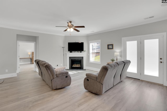 living area with light wood-style flooring, ceiling fan, a fireplace with flush hearth, ornamental molding, and baseboards